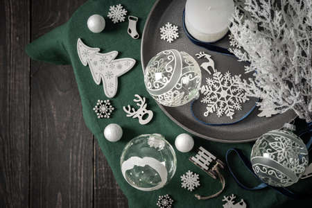 Christmas composition in white and green shades, christmas balls and candle, fir-tree and decorative fir-tree, decoration and snowflakes on a green tablecloth, top view, copy spaceの写真素材
