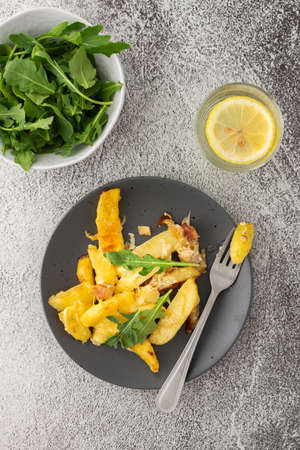 Stewed young potatoes with meat and cheese in a plate with arugula, lemon water in a glass, top viewの写真素材