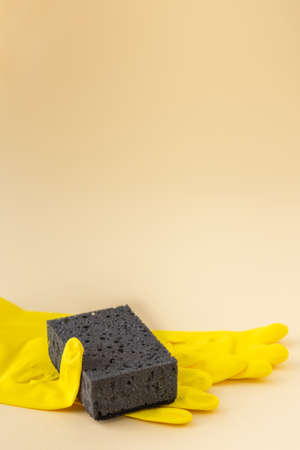 Black dishwashing sponge and yellow rubber gloves on neutral beige background, cleaning conceptの写真素材