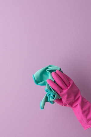 A hand in a pink protective rubber glove holds a microfiber cloth for washing on a purple background