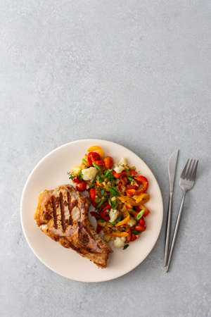 Delicious hearty dinner in plates on the table, fried pork entrecote on the bone with stewed vegetablesの写真素材