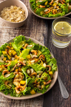 Delicious light dinner, lettuce with fried slices of zucchini, mango and shrimp and almond petals, water with lemon in a glassの写真素材