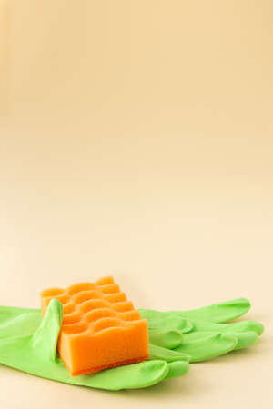Orange dishwashing sponge and green rubber gloves on neutral beige background, cleaning conceptの写真素材