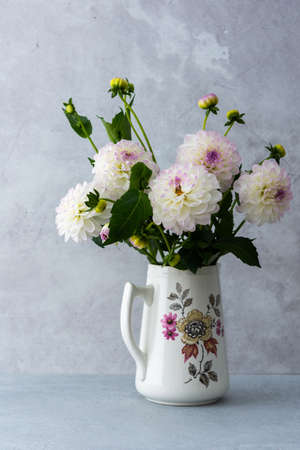 Beautiful autumn bouquet of spherical dahlias in a vase on a table against a background of a gray wallの写真素材
