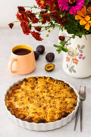 Homemade plum cake with almond flakes, autumn flowers in a vaseの写真素材