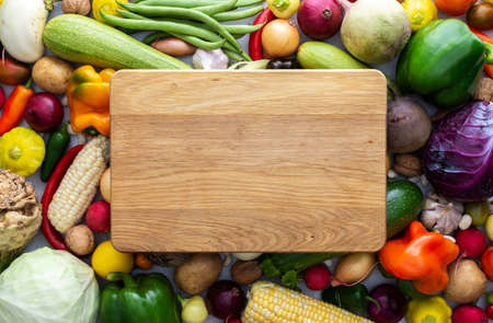 Background with fresh autumn vegetables, rectangular cutting board in the middle of the background, organic healthy farm productsの写真素材