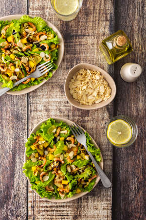 Delicious light dinner, lettuce with fried slices of zucchini, mango and shrimp and almond petals, water with lemon in a glassの写真素材