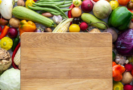 Background with fresh autumn vegetables, rectangular cutting board in the middle of the background, organic healthy farm productsの写真素材