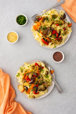 Fettuccine pasta with stewed vegetables, delicious autumn lunch in plates with mustard and fresh green onionsの写真素材