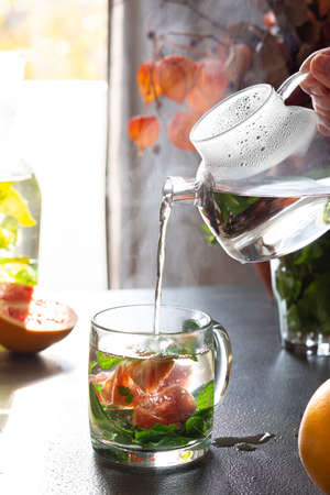 A healthy hot drink with mint and grapefruit, pouring hot water from glass teapot into glasses, aromatic mint tea with citrus fruitsの写真素材