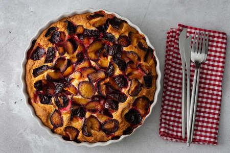 Delicious juicy homemade plum cake in white ceramic tin, cozy autumn table with cake and vase with cranberry, top viewの写真素材