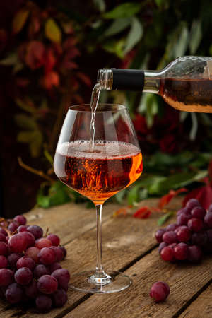 Autumn cozy romantic evening outdoors, wooden table with glass with rose wine, rose wine is poured from the bottle into the glassの写真素材
