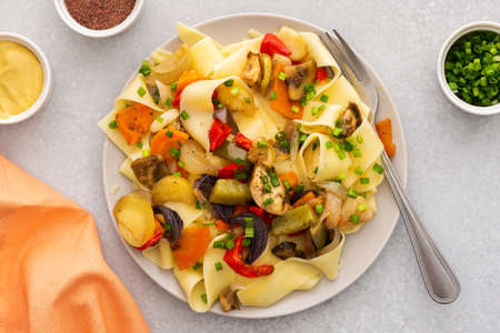 Fettuccine pasta with stewed vegetables, delicious autumn lunch in plate with mustard and fresh green onionsの写真素材