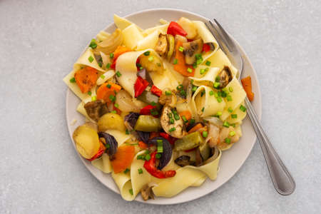 Fettuccine pasta with stewed vegetables, delicious autumn lunch in plate with mustard and fresh green onionsの写真素材