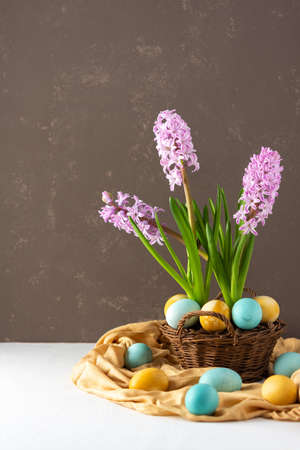 Beautiful pink hyacinths in a wicker basket and blue and yellow painted easter eggs on a gray background, happy easter holidayの写真素材