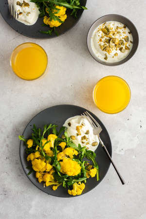 Salad with yellow cauliflower and arugula, Greek yogurt with pumpkin seeds and orange juice, a light healthy breakfast, top viewの写真素材