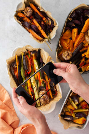 An adult woman takes pictures of stewed vegetables on the phone for social networks or a culinary blog, top view, home cooking hobby, healthy lifestyleの写真素材