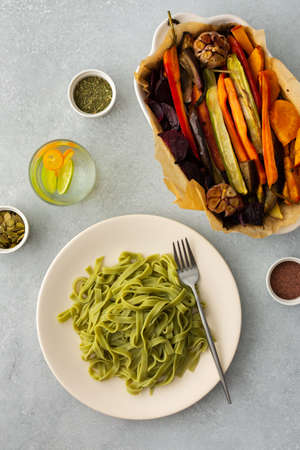 Green pasta tagliatelle with baked vegetables and pumpkin seeds and a glass with water and citrus, top viewの写真素材