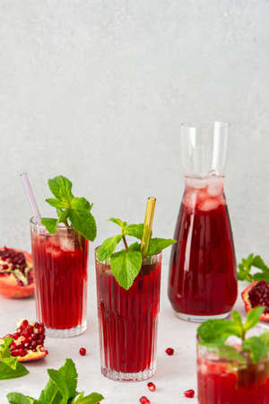 Refreshing pomegranate juice in glasses with mint and glass straw, pitcher of juice and ice, cold drinkの写真素材