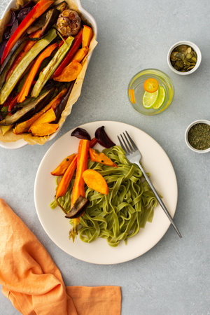 Green pasta tagliatelle with baked vegetables and pumpkin seeds and a glass with water and citrus, top viewの写真素材