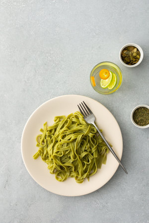 Green pasta tagliatelle with pumpkin seeds and a glass with water and citrus, top viewの写真素材