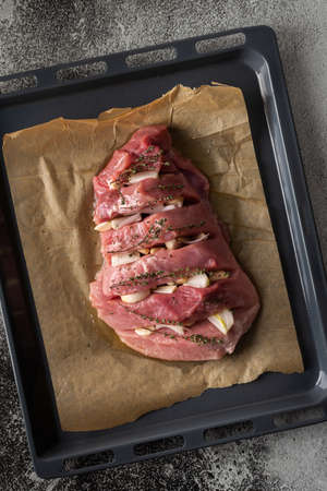 Fresh piece of back of pork with onion, garlic and thyme on parchment paper on a baking sheet, top view of a ready-to-bake piece of meatの写真素材