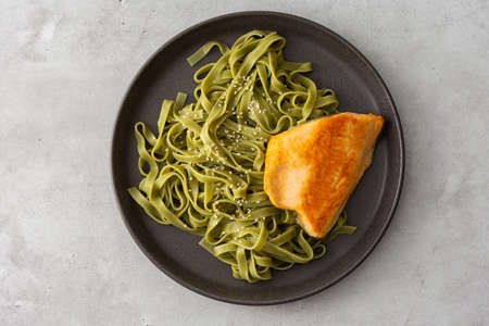 Green pasta tagliatelle with red fish Arctic char , top view of a plate with food, delicious healthy lunchの写真素材