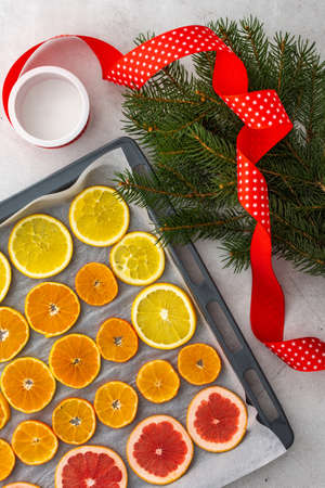 Sliced orange, tangerine and grapefruit slices on baking sheet , spruce branches and ribbon, preparing citrus wedges for Christmas garlandの写真素材
