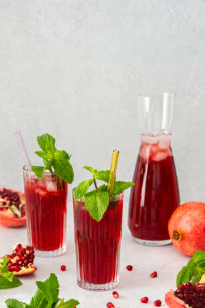 Refreshing pomegranate juice in glasses with mint and glass straw, pitcher of juice and ice, cold drinkの写真素材