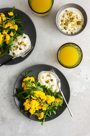 Salad with yellow cauliflower and arugula, Greek yogurt with pumpkin seeds and orange juice, a light healthy breakfast, top viewの写真素材