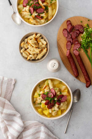 Potato and yellow pea soup with croutons and smoked meats in bowls, cutting board with chopped green onions and smoked sausage, top viewの写真素材