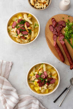 Potato and yellow pea soup with croutons and smoked meats in bowls, cutting board with chopped green onions and smoked sausage, top viewの写真素材