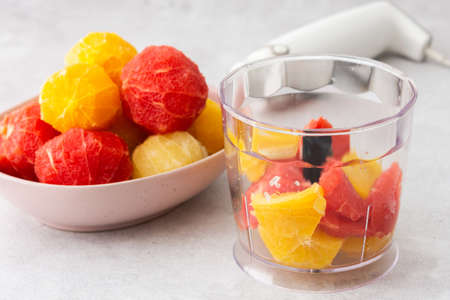 Peeled grapefruits, sweets and oranges in a plate, blender bowl with fruit, making a healthy citrus smoothieの写真素材