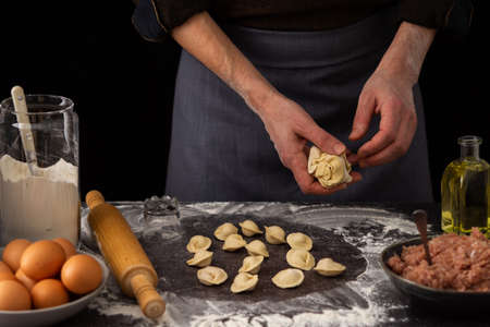 A man sculpts a Russian traditional dish dumplings, milk in a jug and flour, chicken eggs and a plate with minced meat, flour in a jug and olive oilの写真素材
