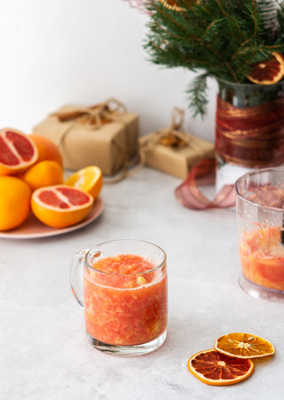 Fresh healthy drink on a festive christmas table, grapefruit and orange smoothie in a glass mug and blender bowl of citrus fruitsの写真素材