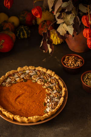 Musk gourd pie garnished with seeds, almond petals and walnuts, autumn table with pumpkins, dried flowers in a vase and a pieの写真素材