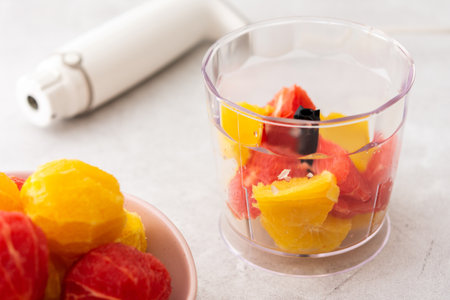 Peeled grapefruits, sweets and oranges in a plate, blender bowl with fruit, making a healthy citrus smoothieの写真素材