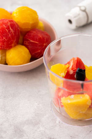 Peeled grapefruits, sweets and oranges in a plate, blender bowl with fruit, making a healthy citrus smoothieの写真素材