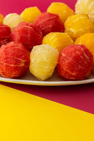 Peeled grapefruits, oroblancos and oranges close-up in an oval dish, view of citrus fruits on a pink yellow backgroundの写真素材
