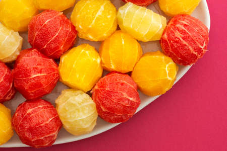 Peeled grapefruits, oroblancos and oranges close-up in an oval dish, top view of citrus fruits on a pink backgroundの写真素材
