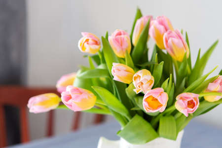 Beautiful spring bouquet of pink tulips in a jug on the table, flowers in a home interiorの写真素材