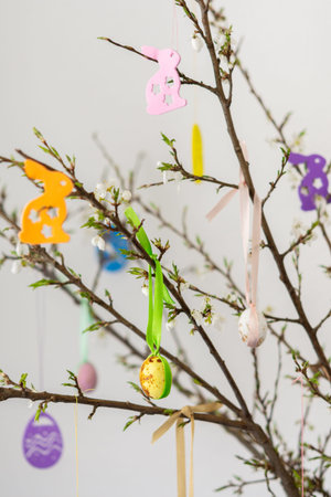 Blooming cherry branches decorated with colorful ribbons with Easter eggs, decorative rabbits, Happy...