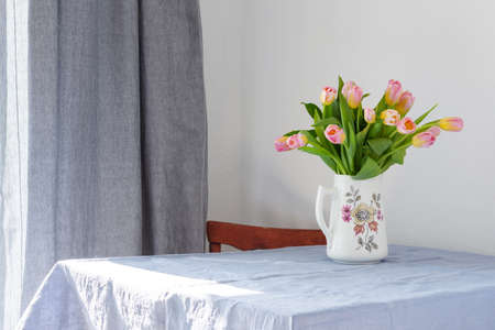 Beautiful spring bouquet of pink tulips in a jug on the table, flowers in a home interiorの写真素材
