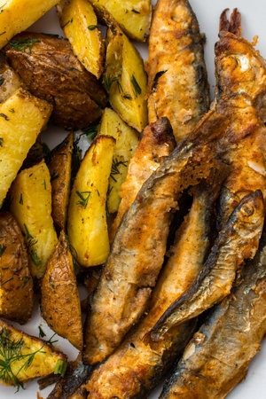 Hearty dinner, baked potatoes with dill and flour-fried capelin close up