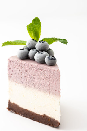 A piece of multi-colored delicious blueberry cheesecake decorated with mint and frozen blueberries close-up on a white backgroundの写真素材