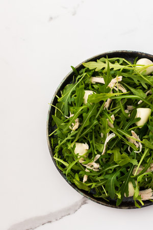 Delicious light salad with arugula, mozzarella and chicken breast in a plate on a white marble background, top viewの写真素材