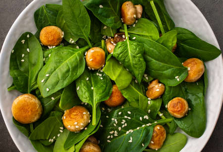 Delicious light salad with spinach and fried champignon mushrooms sprinkled with sesame seeds, top viewの写真素材