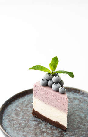 A piece of multi-colored delicious blueberry cheesecake decorated with mint and frozen blueberries close-upの写真素材