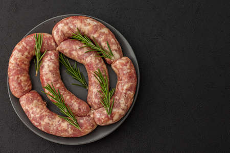 Raw pork sausages with rosemary in a plate close-up on a dark backgroundの写真素材