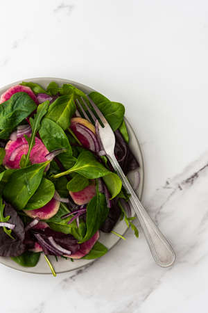 Salad with mix lettuce, red onion and Margelan radish in a plate close-up on a marble backgroundの写真素材